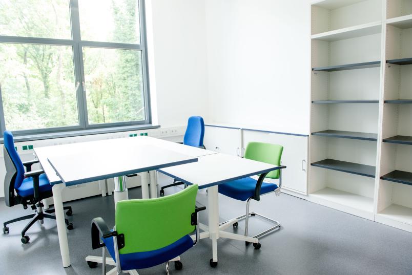 Büroraum mit weißen Tischen und Schreibtischstühlen in grün und blau.