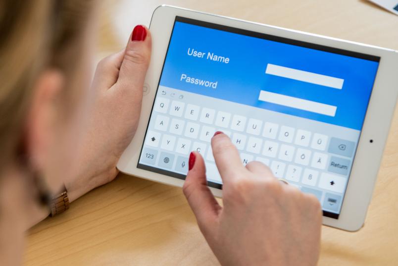 Eine Frau hält ein Tablet in der Hand. Darauf ist ein Feld zur Eingabe eines Passworts zu sehen.
