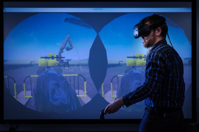 Ein Mann mit Virtual-Reality-Brille bewegt sich vor einer Projektionsfläche.