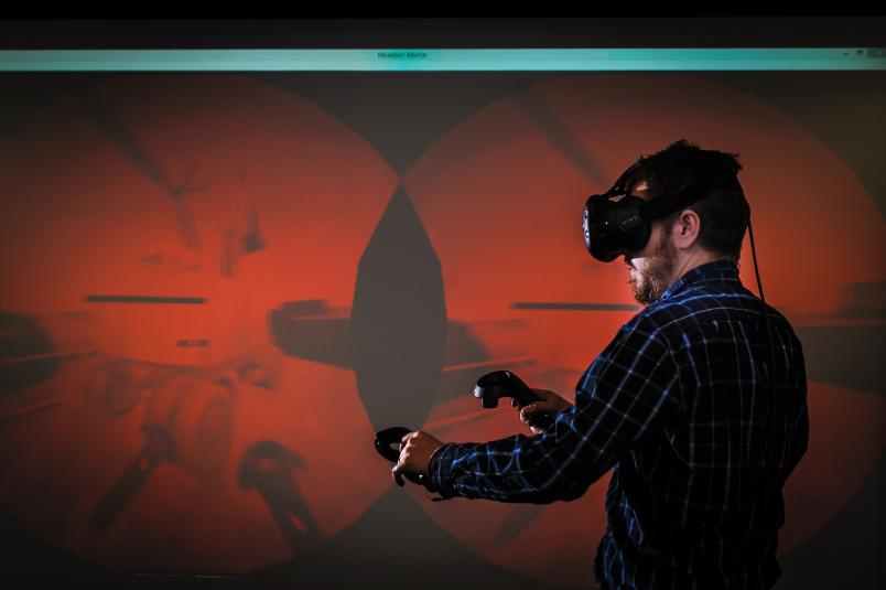 Ein Mann mit Virtual-Reality-Brille bewegt sich vor einer Projektionsfläche.