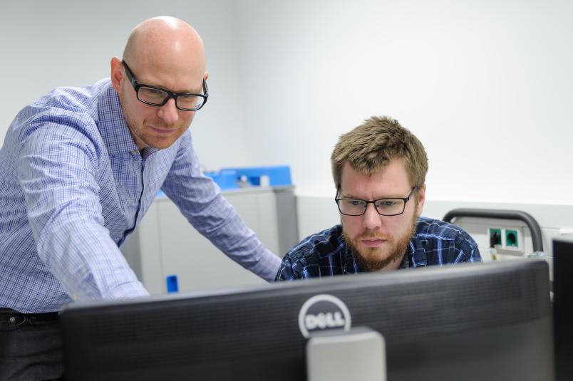 Zwei Männer blicken auf einen Computer.