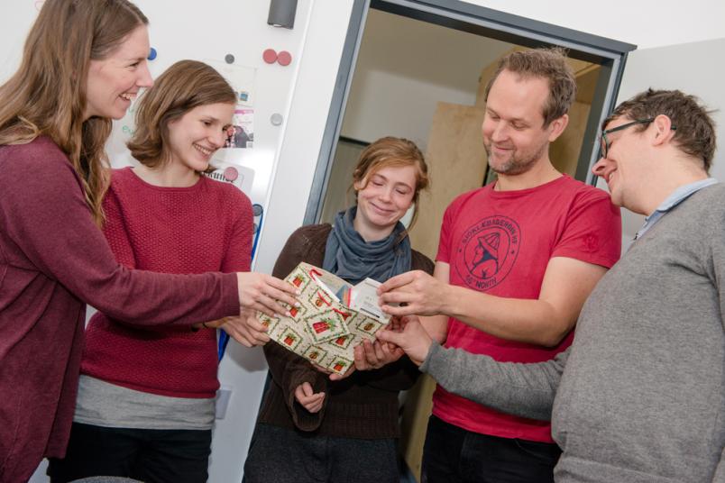 Drei Frauen und zwei Männer beugen sich über eine weihnachtliche Geschenktüte.