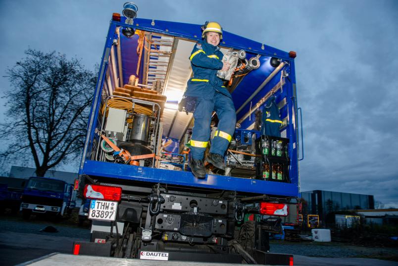 Frau in Uniform springt aus einem Einsatzwagen des Technischen Hilfswerk.