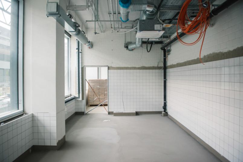 Ein Raum im Rohbau mit frischem Beton auf dem Boden und weißen Fliesen an der Wand