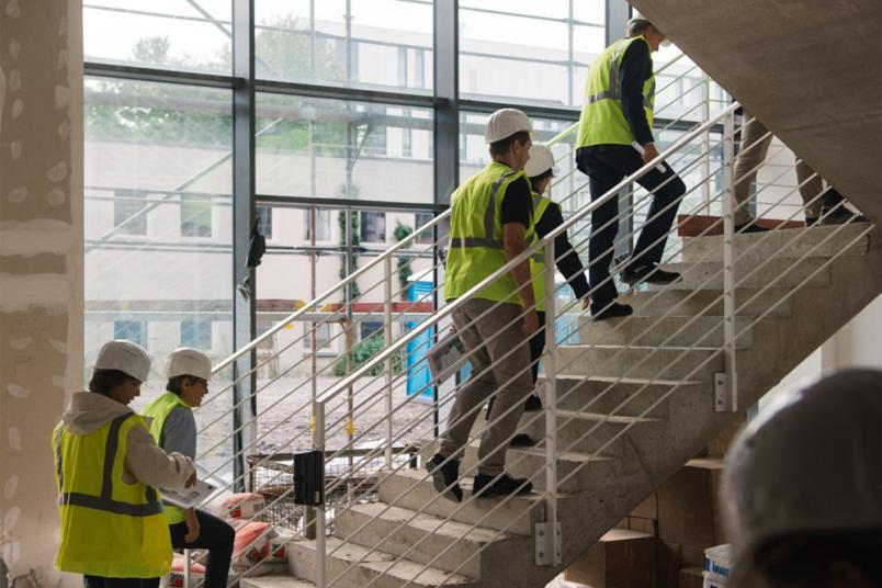 Menschen gehen eine Treppe im Rohbau hoch.