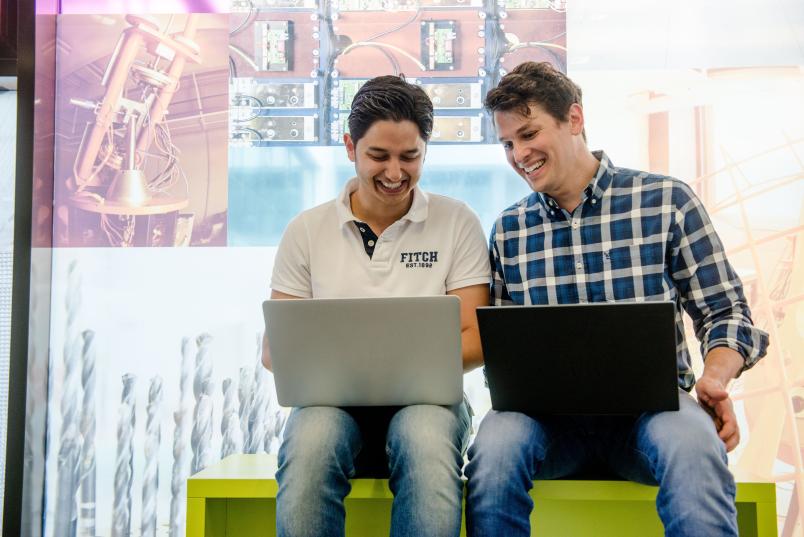 Zwei Männer lachen und haben ihre Laptops auf dem Schoß