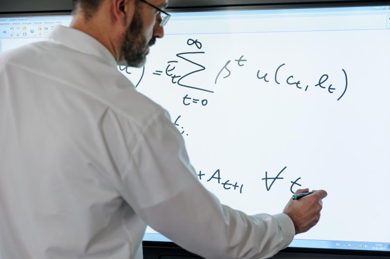 Ein Mann schreibt Formeln an ein Smartboard.