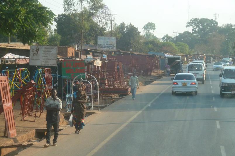 Blick aus einem Bus auf eine Straße in Malawi, neben der sich Verkaufsstände reihen.