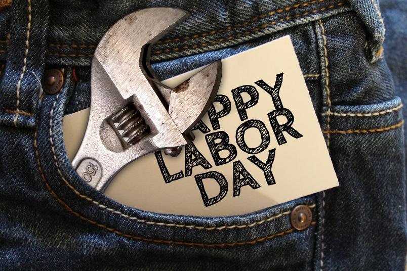 In der Gesäßtasche einer Jeans stecken ein Schraubschlüssel und ein Sticker mit der Aufschrift „Happy Labor Day“