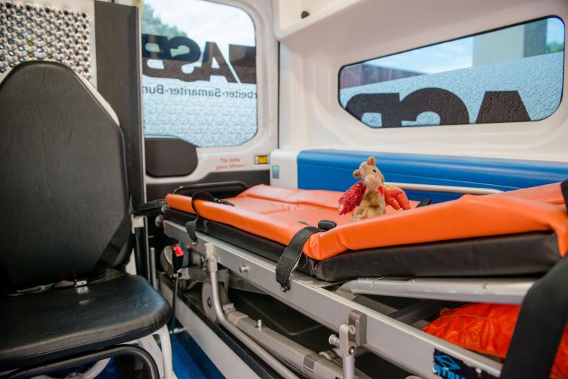 Der Kuscheltier-Drache sitzt auf einer Trage in einem Rettungswagen.
