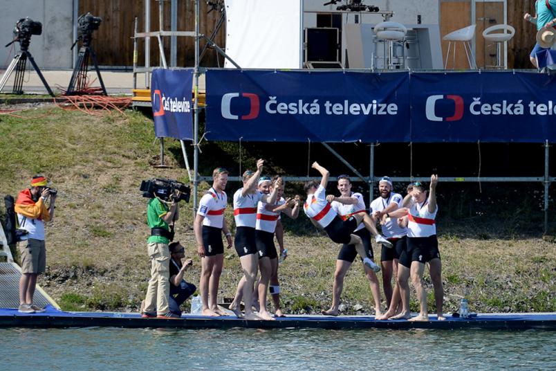Männer auf einem Steg schmeißen einen Mann freudig ins Wasser