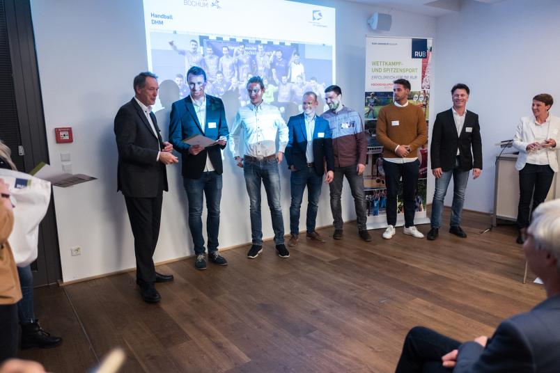 Mehrere Männer stehen mit dem Rücken zur Wand in einer Projektion