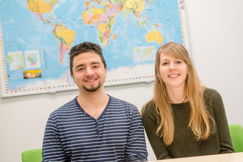 Ein Student und eine Studentin sitzen vor einer Weltkarte.