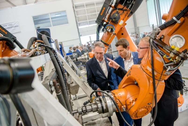 Der Rektor und der Oberbürgermeister bekommen von Bernd Kuhlenkötter eine kleine Führung und Erläuterungen aus erster Hand – hier zu Robotern, die Bleche verformen.