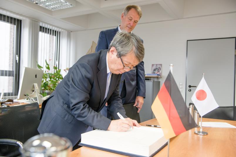 Masashi Haneda, Vizepräsident der Universität Tokio (vorn), trägt sich im Büro von Rektor Axel Schölmerich in das Gästebuch der RUB ein.