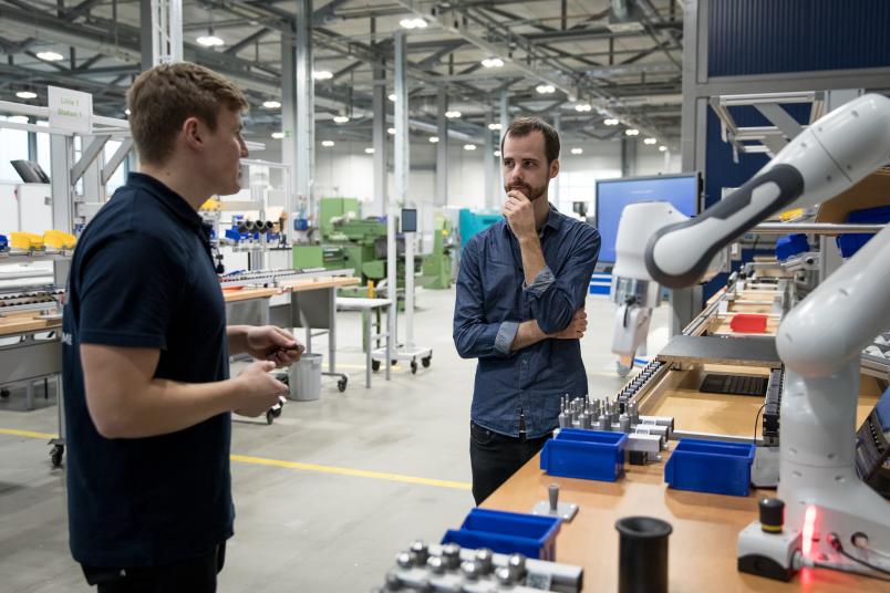 Zwei Männer stehen vor einem Roboter und reden.