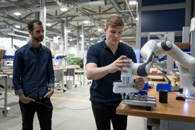 Ein Mann steuert einen Roboter. Ein anderer Mann steht daneben und schaut zu.