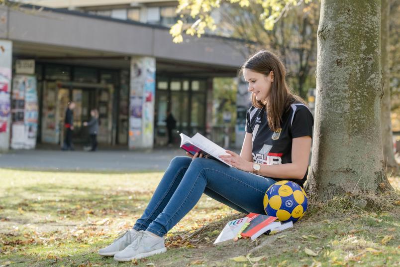 Studentin sitzt unter einem Baum und lernt