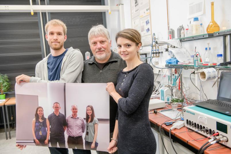 Dreiergruppe hält ein großes Foto in den Händen