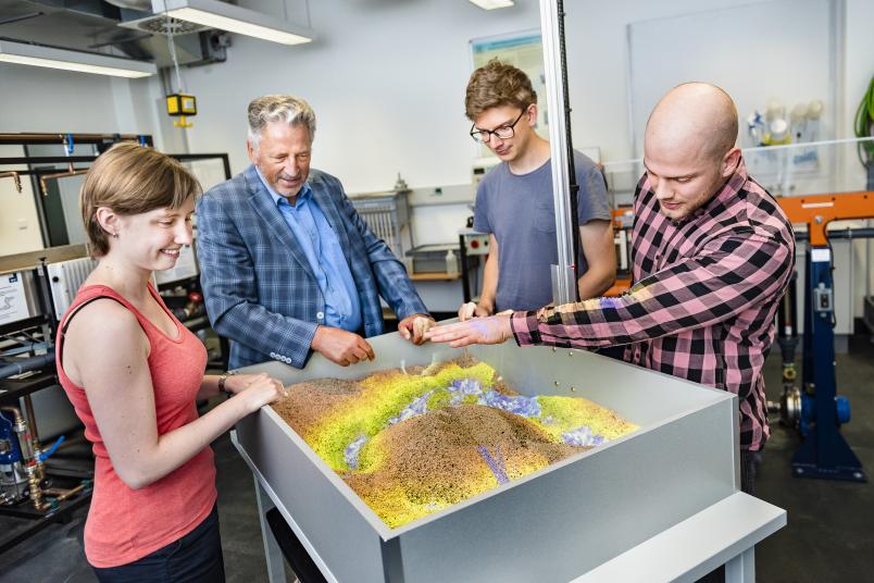 Kiste mit Sand, auf den bunte Höhenlinien projiziert sind, umringt von Menschen