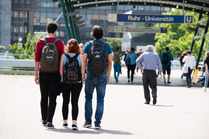 Drei Personen laufen auf der Unibrücke Richtung Haltestelle.