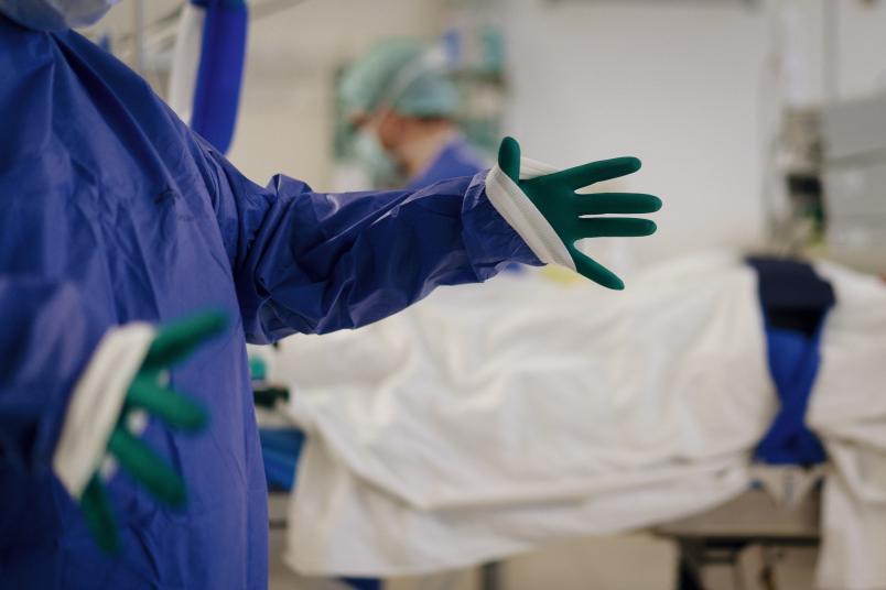 Blick in einen Operationssaal, in dem sich jemand Handschuhe und Kittel anzieht