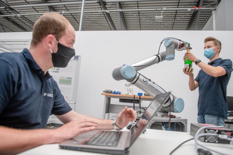 Forscher gibt Roboter eine Sektflasche in den Greifarm.
