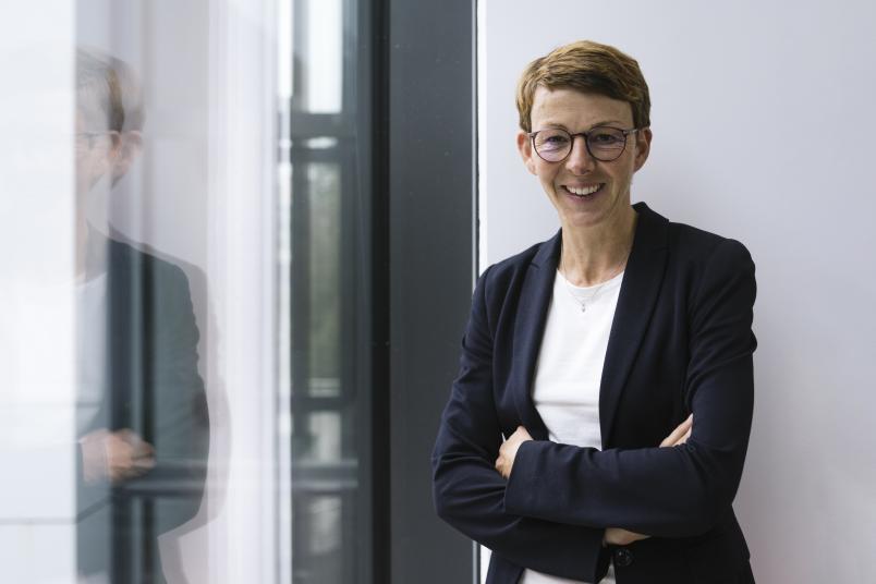 Eine Frau in schwarzem Blazer steht lachend an einem Fenster
