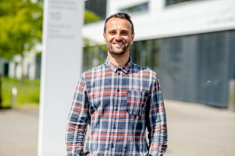 Ein Mann im Karohemd steht in der Sonne und lacht