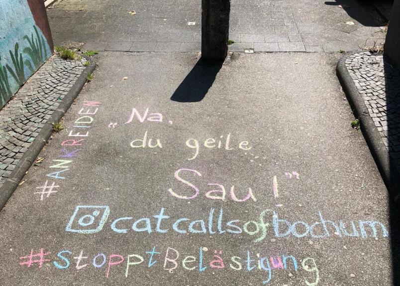 In bunter Schrift steht auf dem Boden geschrieben "#Ankreiden", "Na, du geile Sau!", "@catcallsofbochum" und "StopptBelästigung"