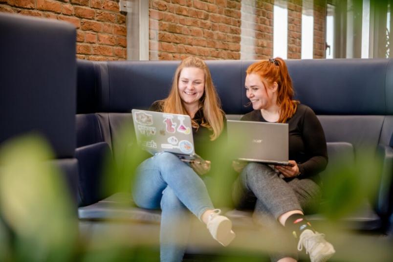 Zwei Studentinnen sitzen auf einer Couch nebeneinandern und schauen auf einen Laptop.