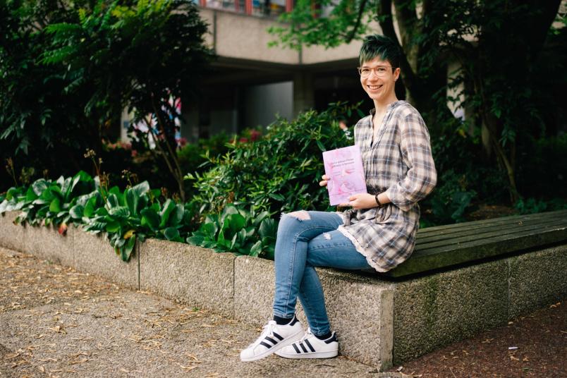 Studentin sitzt und hält ein Buch in der Hand.