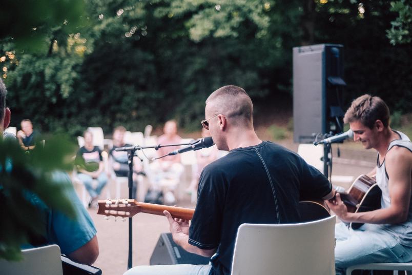 Von hinten fotografiert: Zwei Musiker spielen auf einer kleinen Bühne Gitarre und singen in Mikros