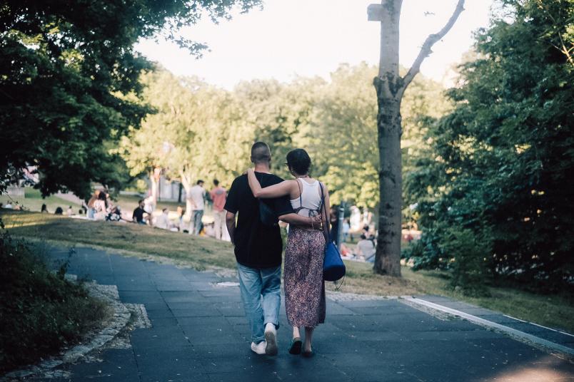 Zwei Menschen laufen Arm in Arm unter Bäumen her