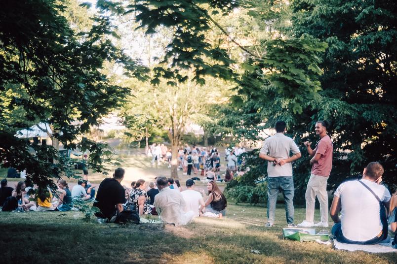 Viele Menschen sitzen auf Decken auf einer abschüssigen Wiese, einige stehen.