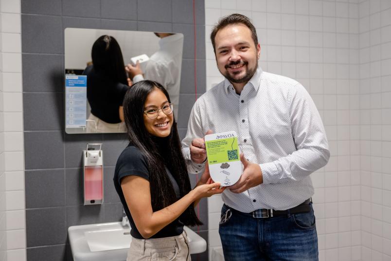 Zwei Personen in einem WC mit einem Tamponspender in der Hand.