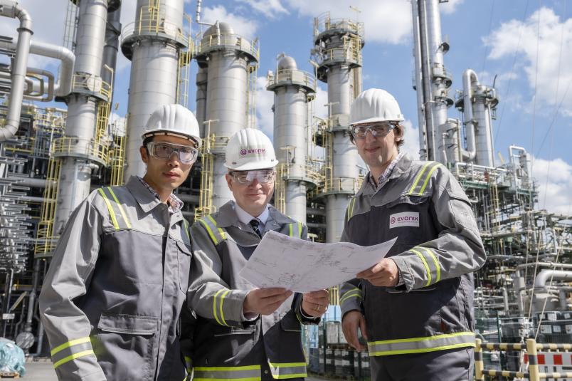 Drei Personen vor einer industriellen Anlage
