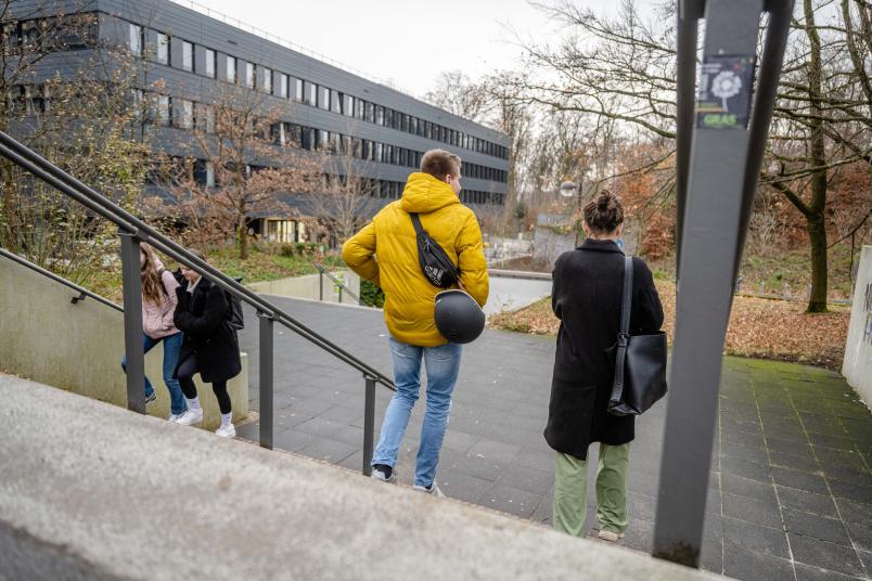 Zwei Personen gehen eine Treppe runter. Im Hintergrund ist das Gebäude GD. Die Personen sind von hinten zu sehen.