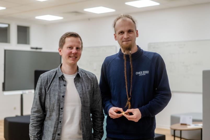 Zwei Personen, eine hält einen winzigen goldenen Chip in den Händen.