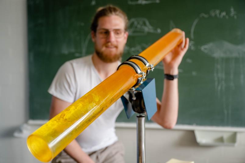 Eine Plexiglasröhre mit einer gelben und orangenen Flüssigkeiten, die verwirbeln.