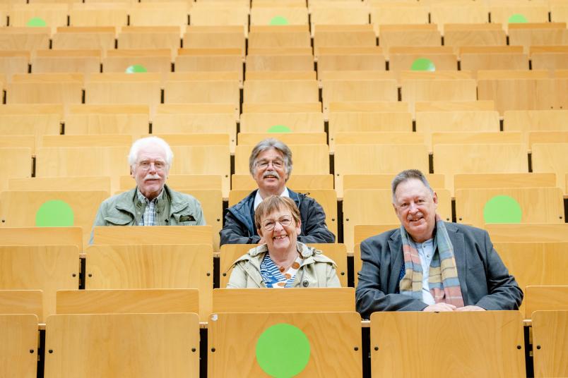 Eine Gruppe von vier ehemaligen Studierenden sitzen im Hörsaal