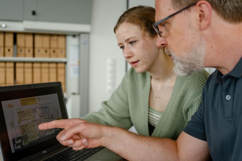 Mann zeigt junger Frau etwas auf Laptopbildschirm