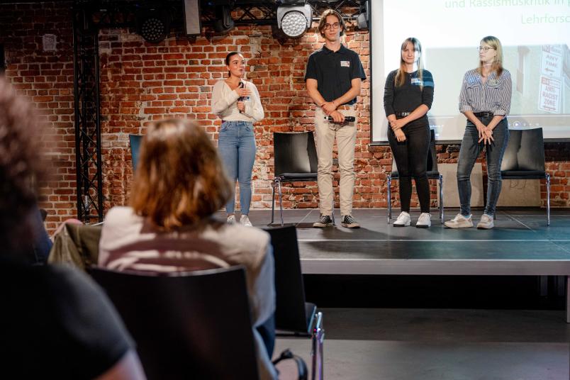 Vier Studierende auf der Bühne. Sie haben ihre Forschungsergebnisse zum Thema Rassismus vorgestellt.