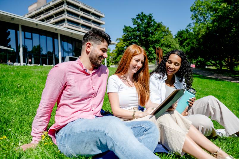 3 Studierende auf Wiese vor Qwest