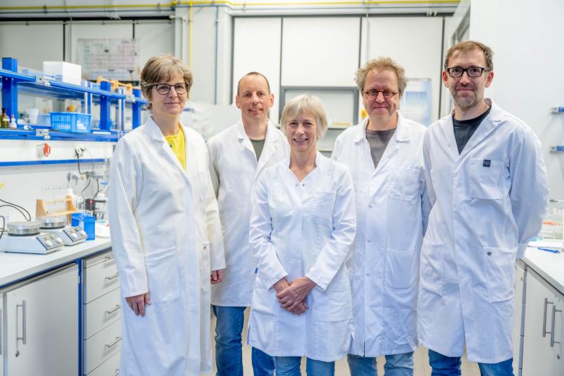 fünf Personen mit Kitteln stehen in einem Chemielabor.