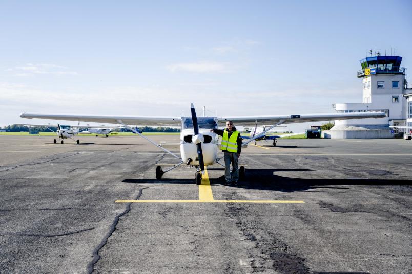 Eine Person in Warnweste vor einem kleinen Flugzeug auf einem Flugplatz