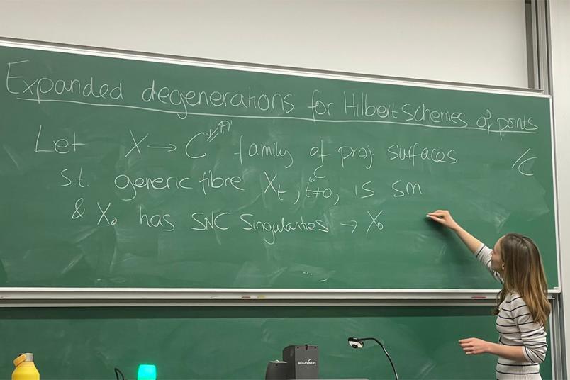 Eine Person schreibt mathematische Formeln an eine Tafel in einem Hörsaal,