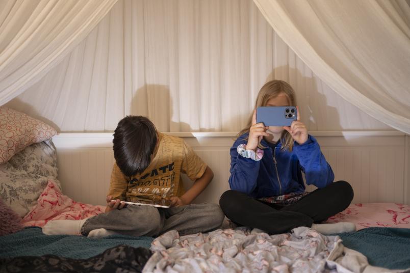 Zwei Kinder mit Tablet und Smartphone auf einem Bett