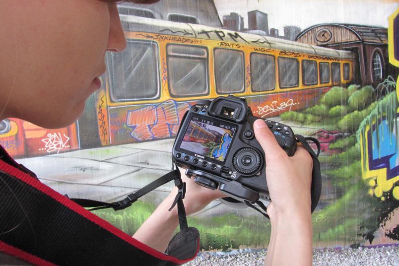 Hand hält Kamera, im Hintergrund Leinwand mit buntem Zug