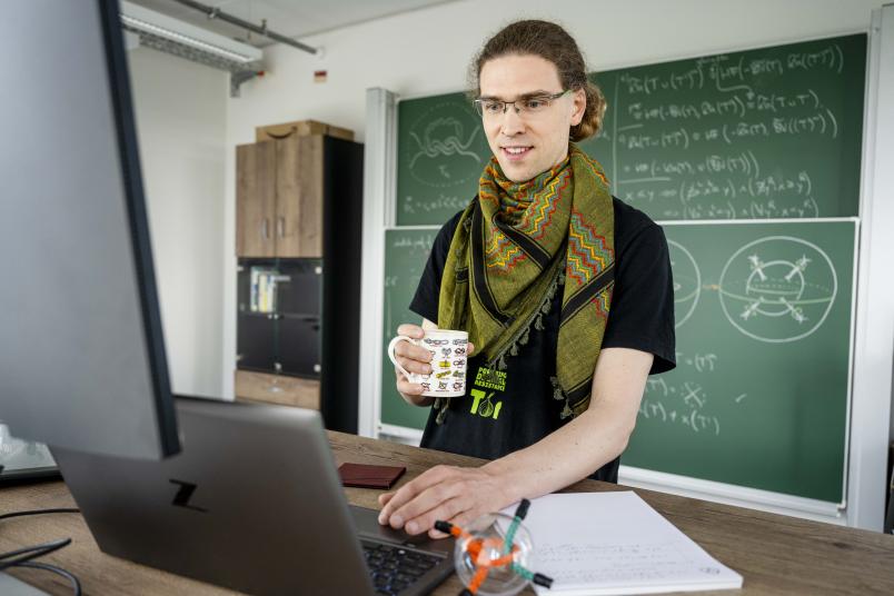 Eine Person mit einer Kaffeetasse in der Hand, auf der verschiedene Knoten zu sehen sind, arbeitet am Computer.